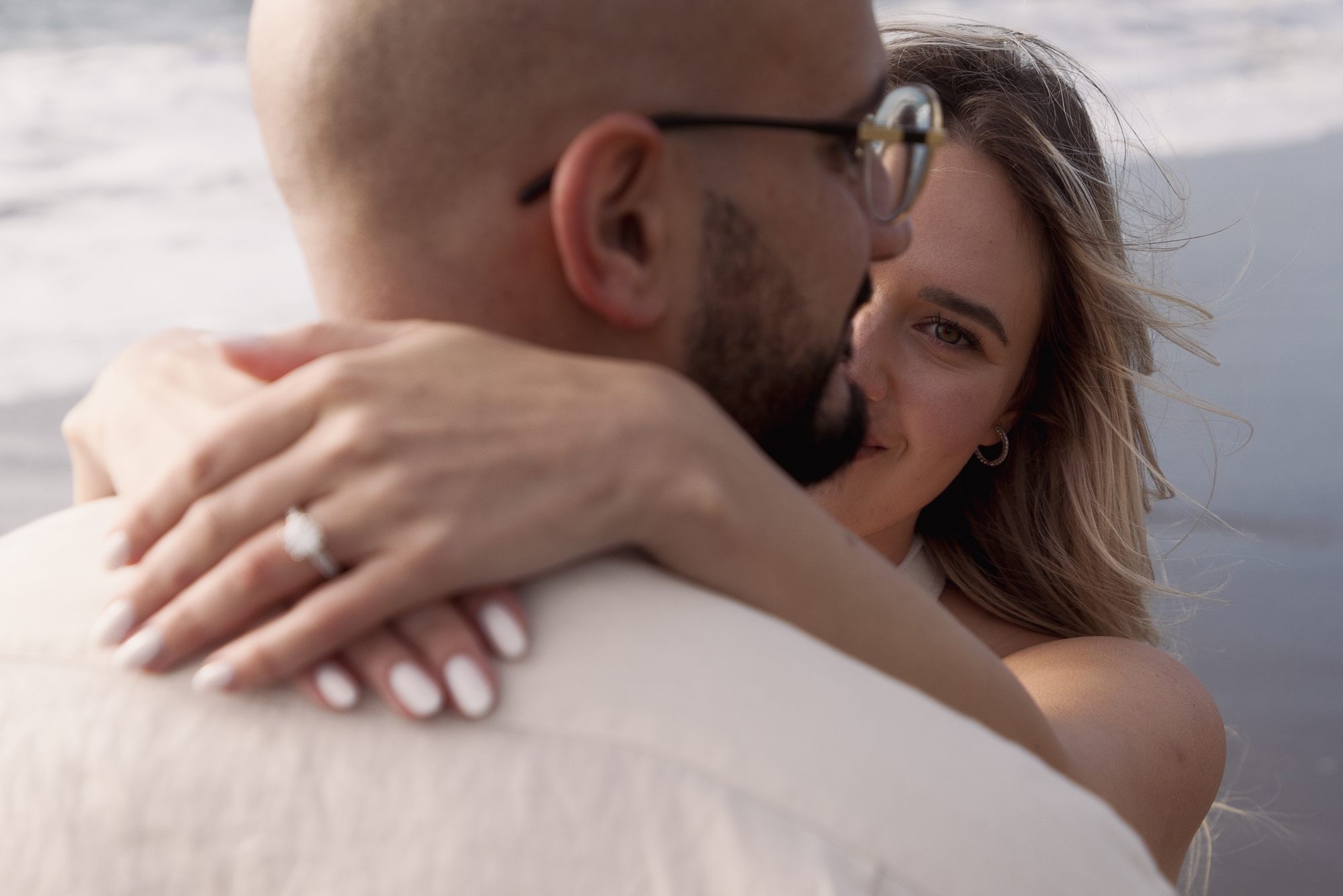 She smiles over his shoulder, ring in frame