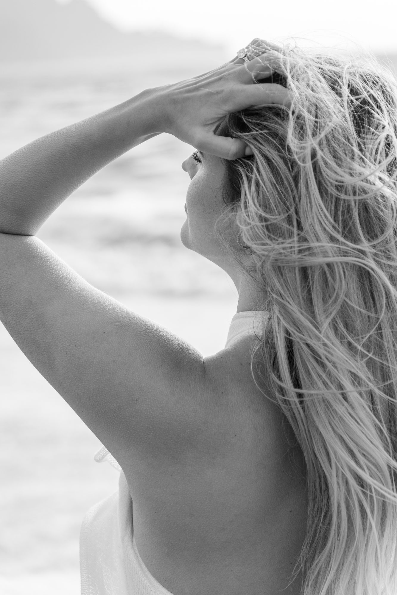 Black and white close-up, woman looking up, hand in wind-blown hair