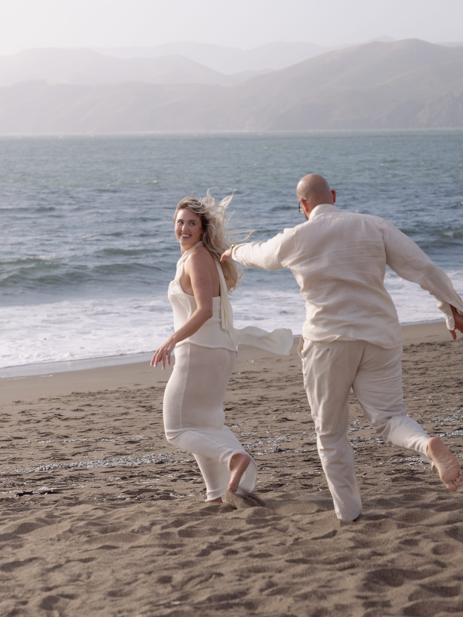 She laughs back as he chases her down the beach