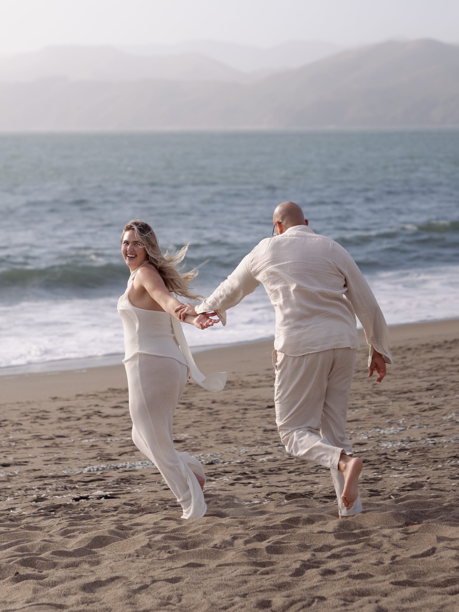 Couple running hand in hand on Baker Beach